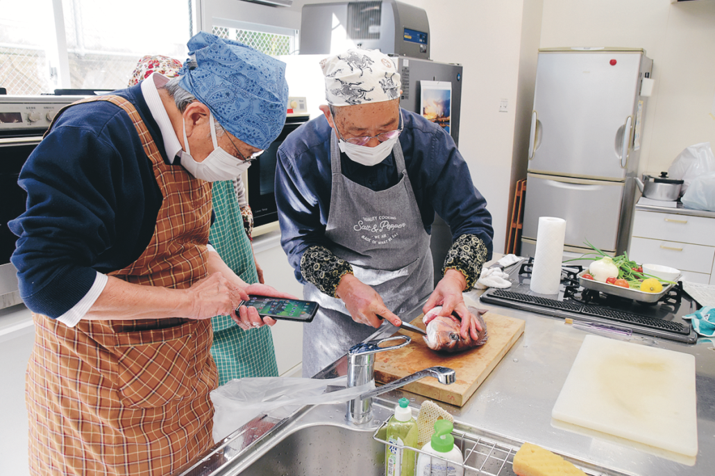 魚さばき隊の包丁さばきをスマホで撮影する参加者も（南郷コミセン）